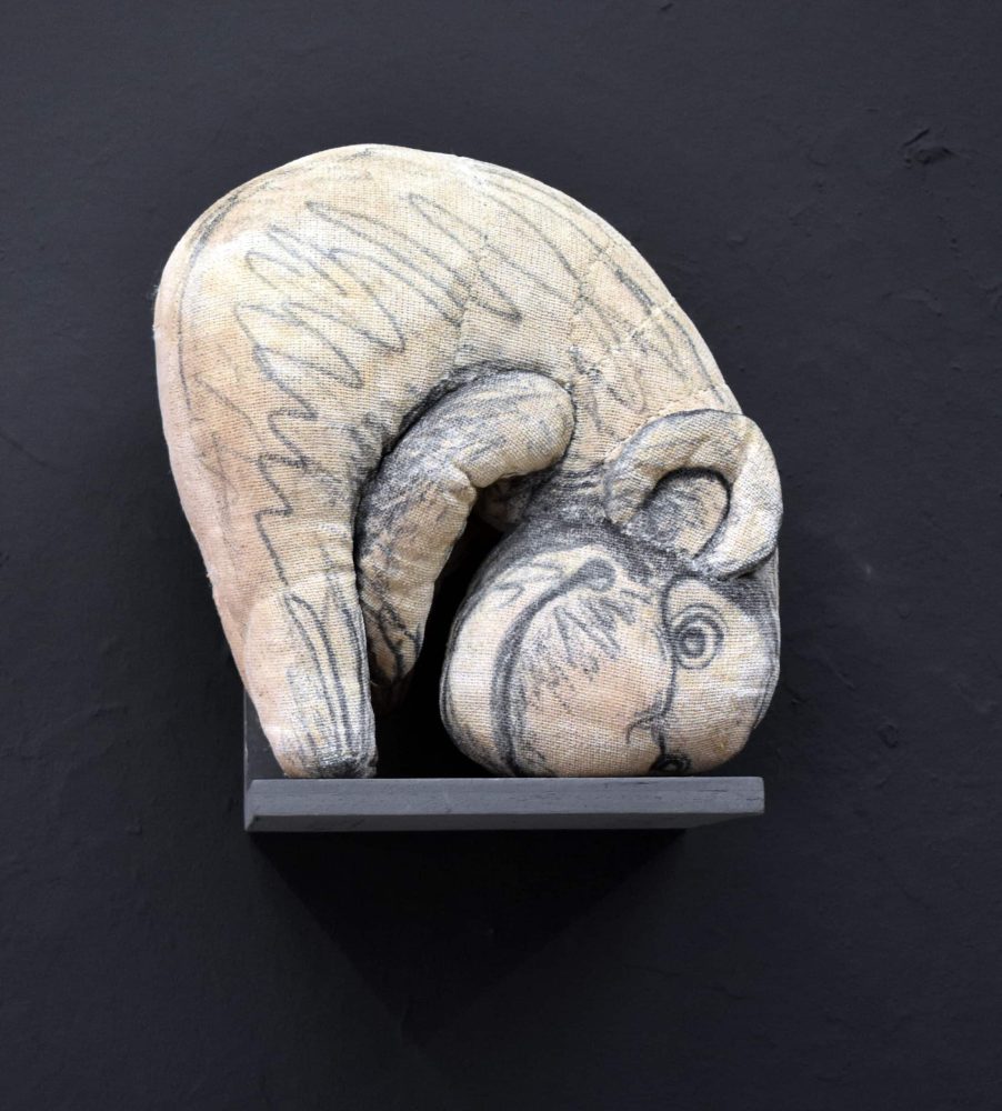 Detail view at Galerie Daeppen, Basel, of a curled textile figure drawn with black marker lines, folded tightly over itself on a dark wall-mounted shelf.