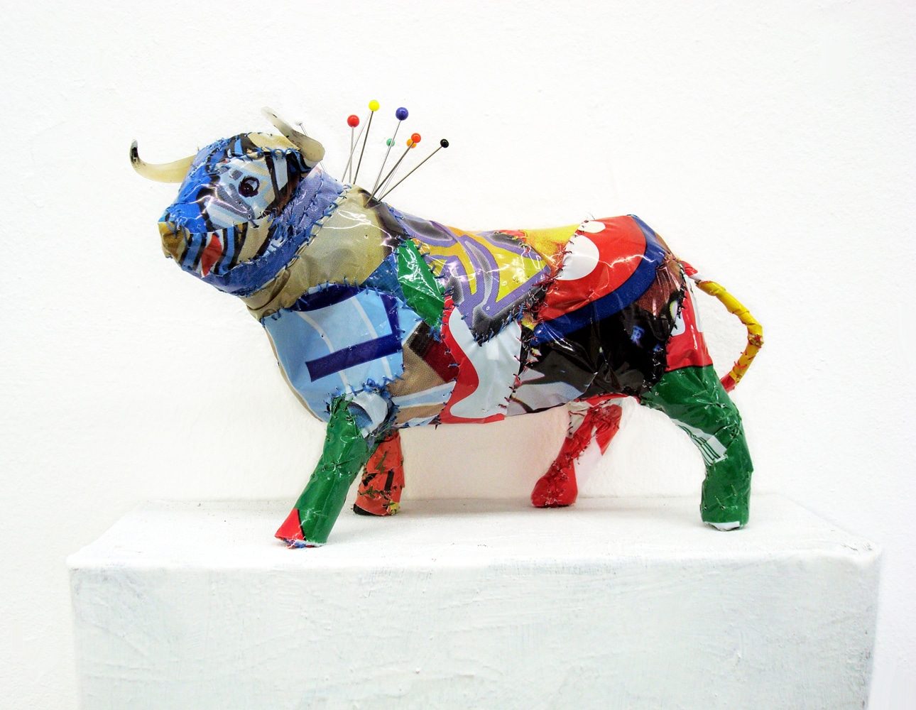 Bull sculpture covered in printed plastic bags, with pins inserted into its neck in reference to bullfighting.
