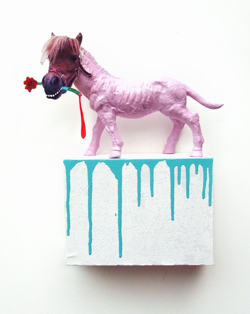 Pink painted toy pony with a flat wooden head, standing on a white wooden box with blue paint dripping down the front.