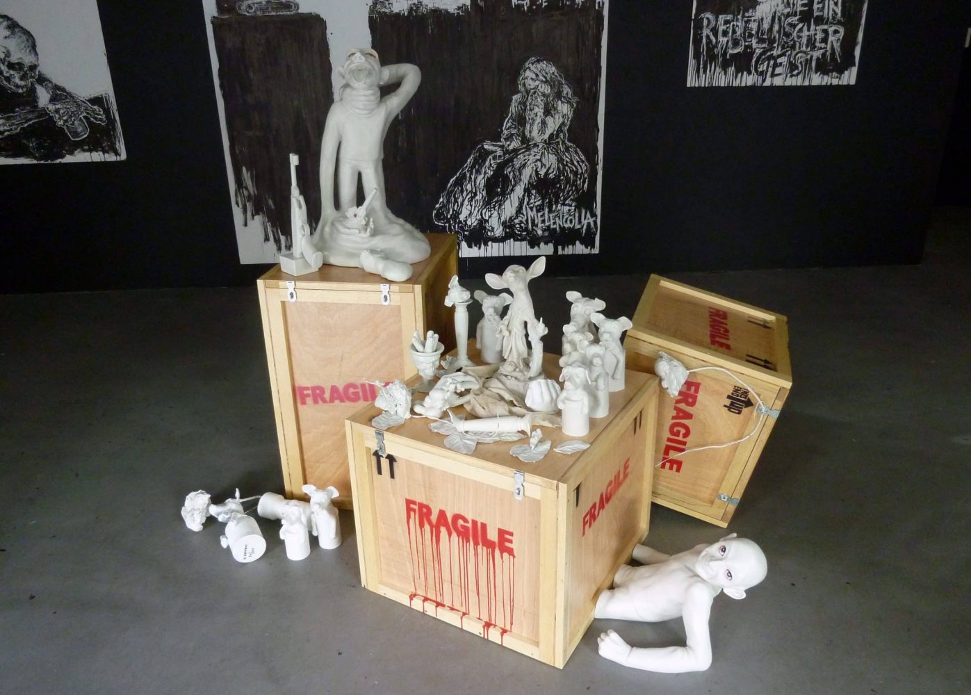 Installation view of white sculptural figures arranged around wooden transport crates marked FRAGILE.