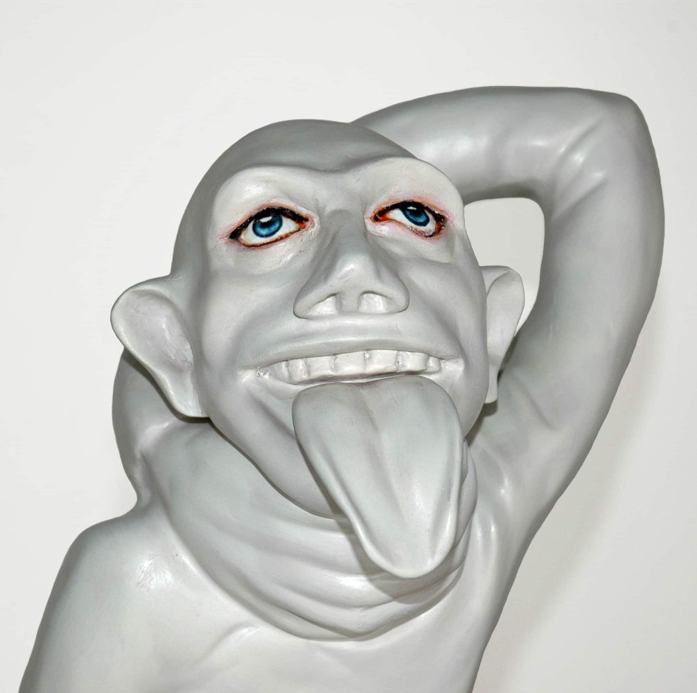 Close-up of a pale sculptural figure with red eyes, its arm raised behind its head.