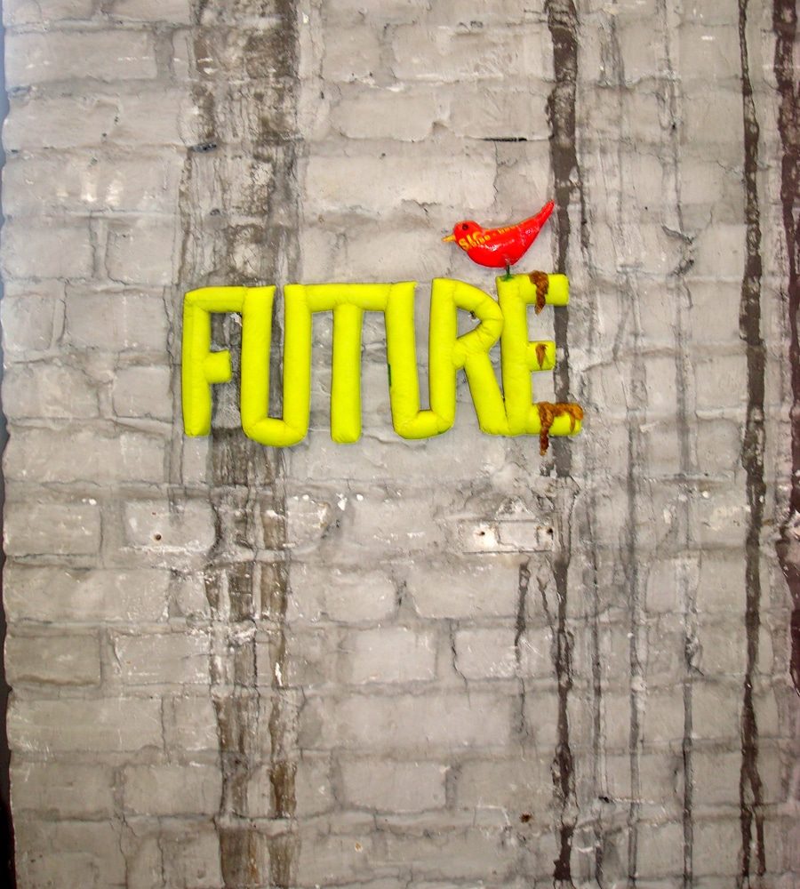 Wall-mounted painted plastic work spelling “FUTURE”, with a small bird defecating on the word.
