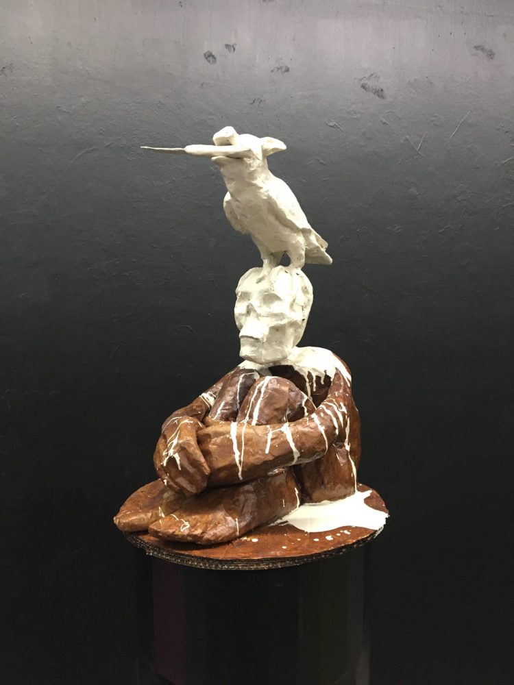 Human-like figure with a skull head carrying a bird holding a knife in its beak.