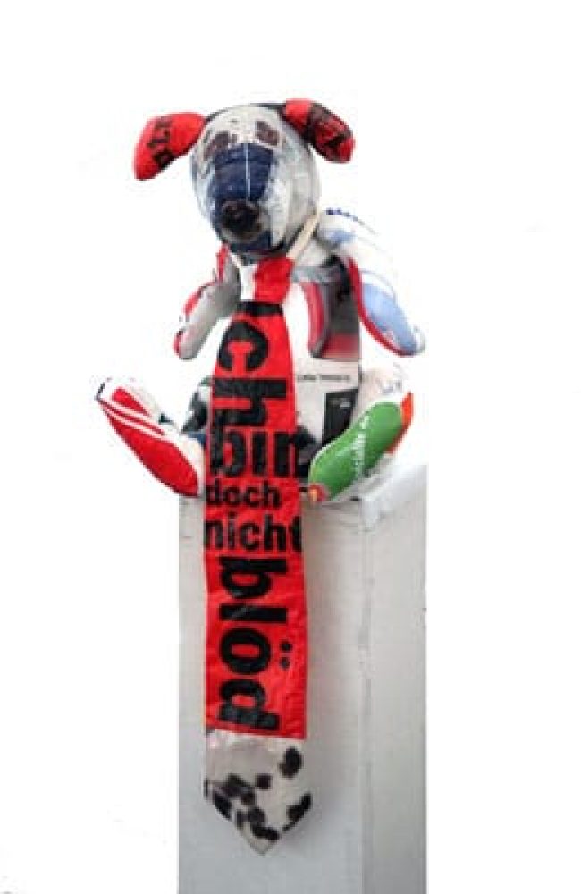 Seated dog-like figure sewn from discarded plastic shopping bags, wearing a tie reading “Ich bin doch nicht blöd”.