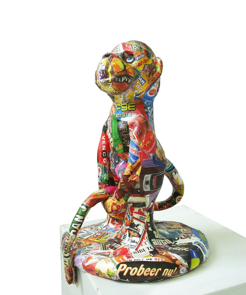 Standing monkey-like figure holding its tail in its hands, displayed on a pedestal.