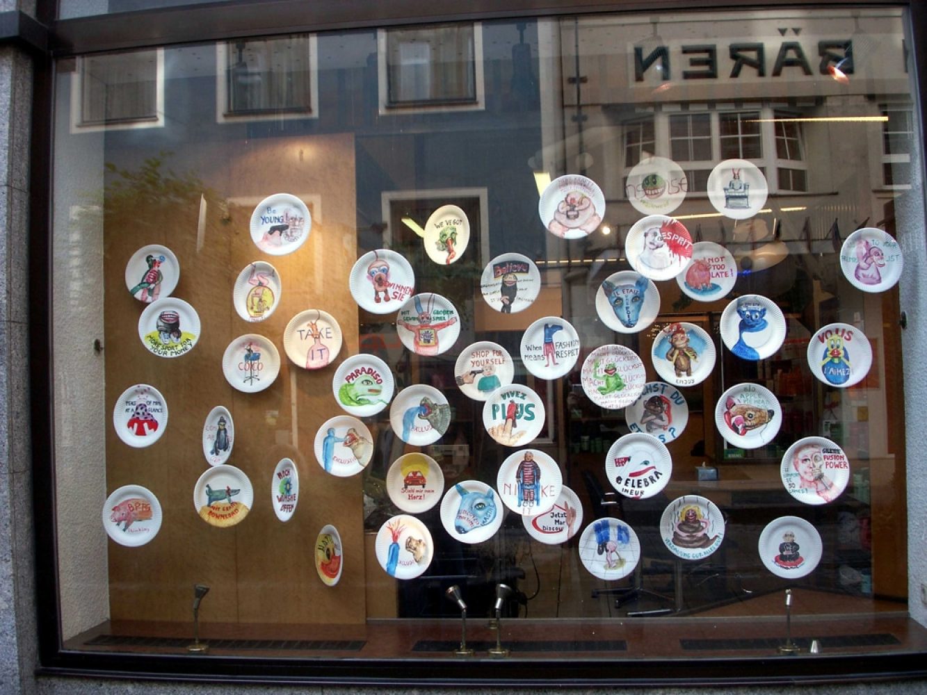 Paper-plate works from the Macht glücklich series installed across a commercial shop window in Linz.