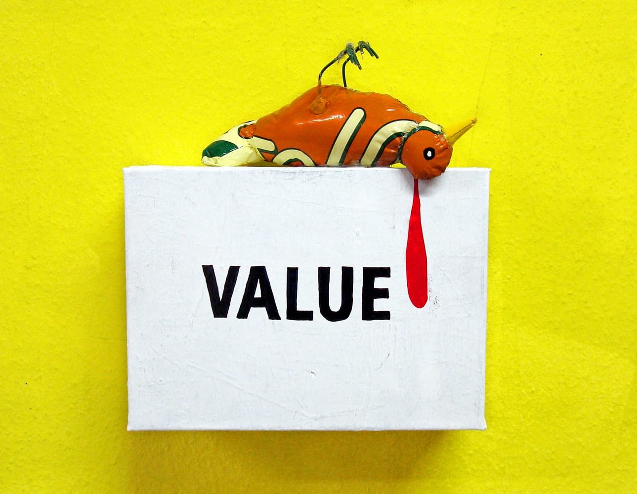 Wall-mounted white box with a small dead bird made from plastic lying across the top, and the word “VALUE” on the front.
