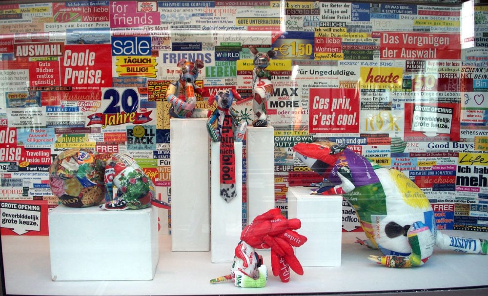 Sculptural works installed in a commercial shop window against a dense backdrop of advertising material.