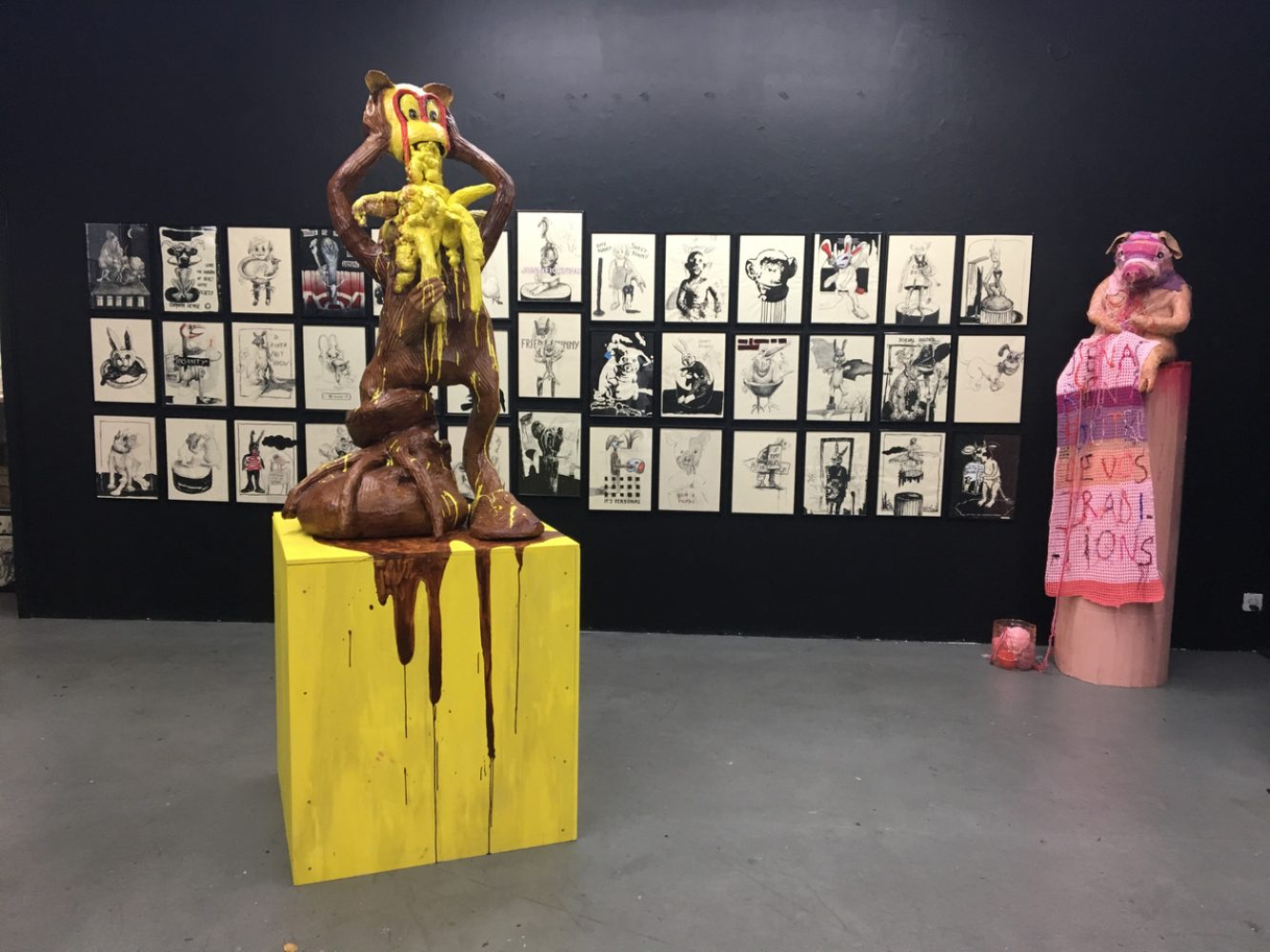 Installation view with a yellow and pink sculptural figure and a wall of framed drawings at Sweet Bunny Cute Bunny, Basel.