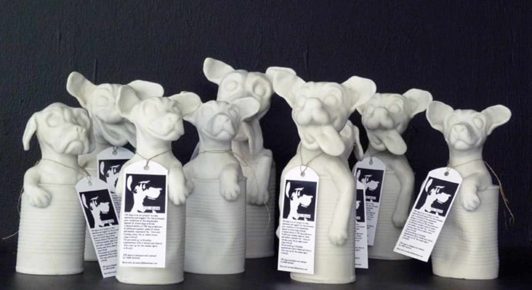 Group of white 250DOGS sculptures with hanging labels.