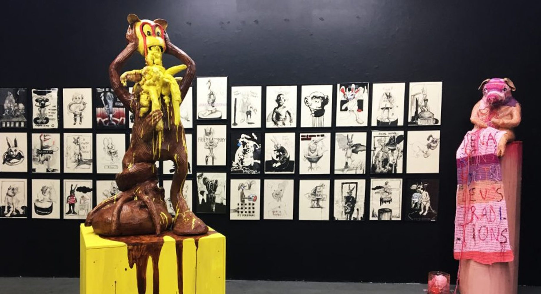 Installation view with a yellow and pink sculptural figure and a wall of framed drawings at Sweet Bunny Cute Bunny, Basel.