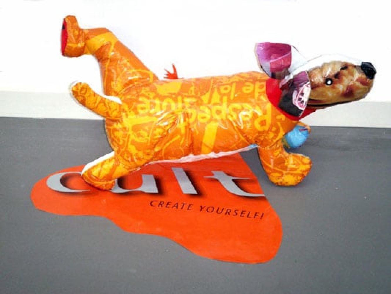 Colourful dog sculpture made from plastic shopping bags urinating against a wall.
