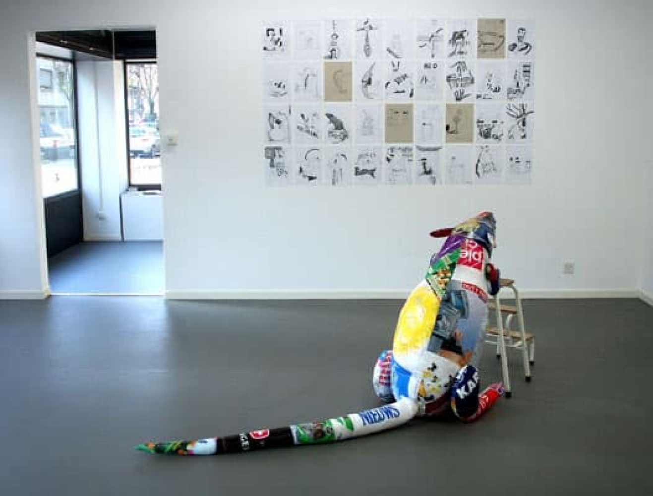 Exhibition view of Synthetic Ivory with a large rat sculpture made from plastic shopping bags leaning against a small stepladder.