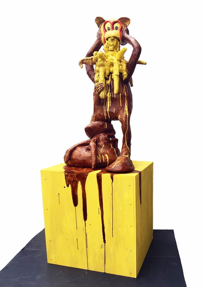 Human-like figure with a red M on its head pulling off its own head as yellow matter spills out.