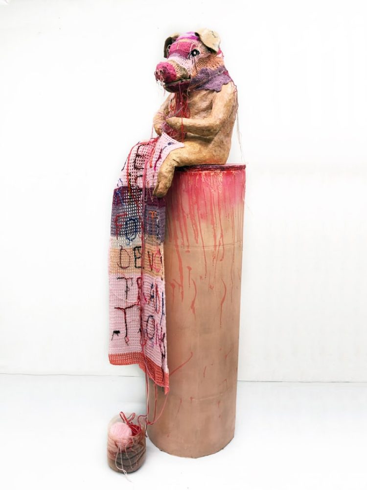 Full view of Rien à foutre, a tall pink pig-like figure seated on a pedestal with crochet extending down the front.