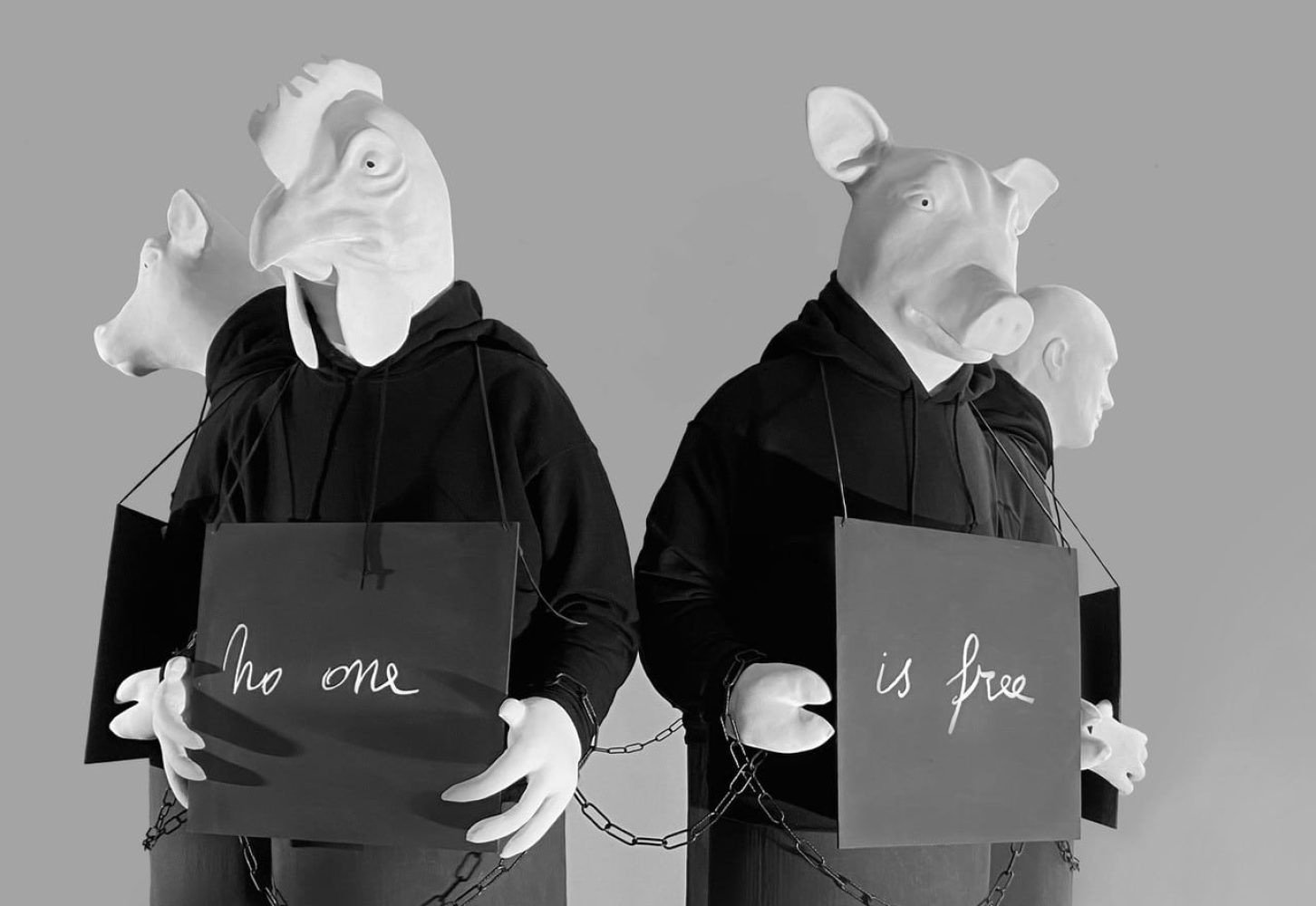 Detail of sculptural figures from Until We All Are Free, holding signs with text fragments, their hands chained together.